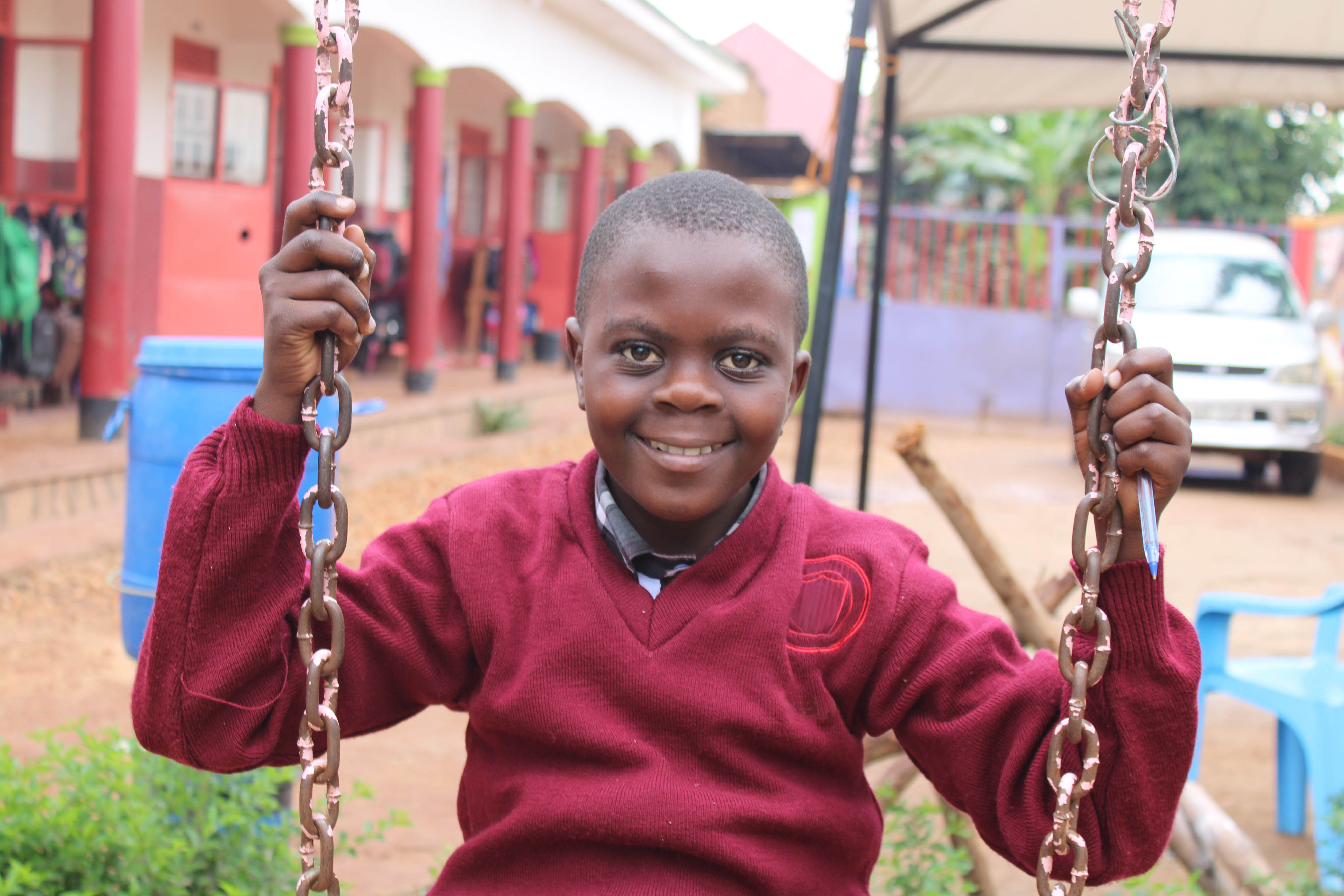 Boy is smiling at the camera while sitting on a swing