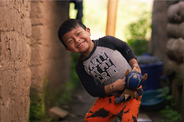 A young boy is grinning broadly as he plays with his Paw Patrol stuffed dog. His shirt says, "Party at my crib."