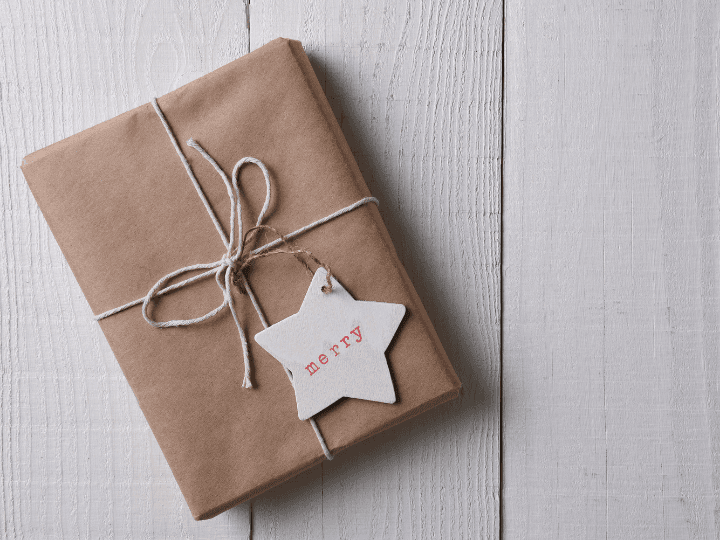 A present wrapped in brown paper, tied with a string. Attached is a gift tag shaped like a star with the word "merry" on it.