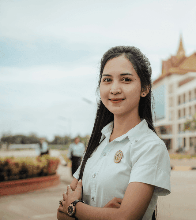 A female college student standing in front of the backdrop of her university
