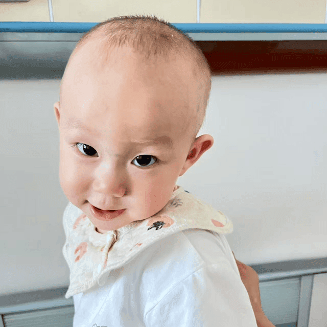 Dressed in white, a baby boy in LWB's cardiac program smiles and looks intently into the camera.