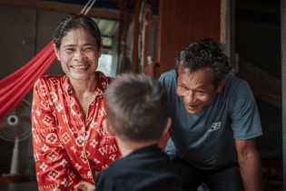 Foster parents laugh and play with their foster son, whose back is to the camera. 