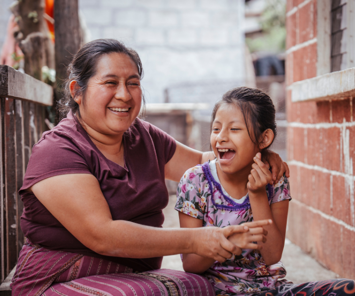 A young Guatemalan girl is laughing with an older woman.