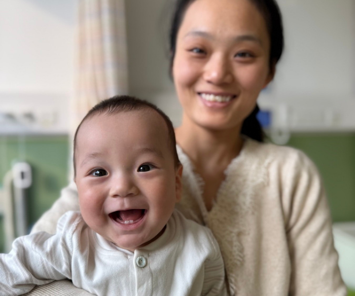 Mother holding her baby boy, who smiles widely, showing his two new bottom front teeth.
