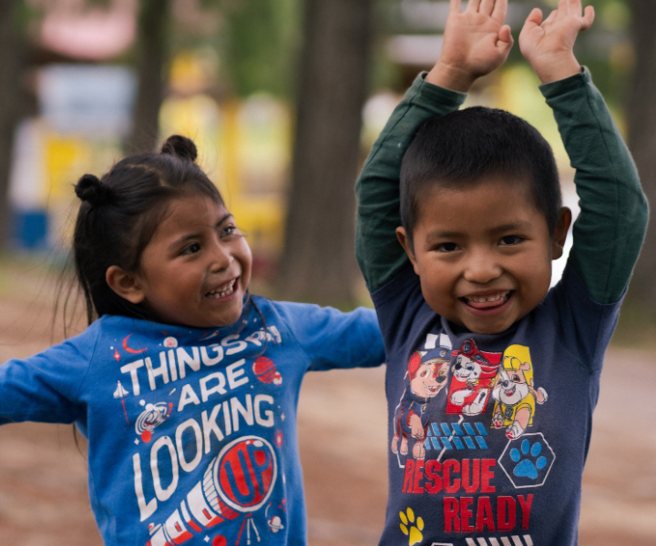 A boy and a girl laugh and play together. The boy is smiling at the camera.