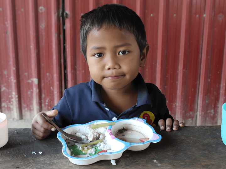 A young boy from Cambodia finishes up his meal. There is still some rice left on his plate. He wears LWB's navy blue school uniform. 