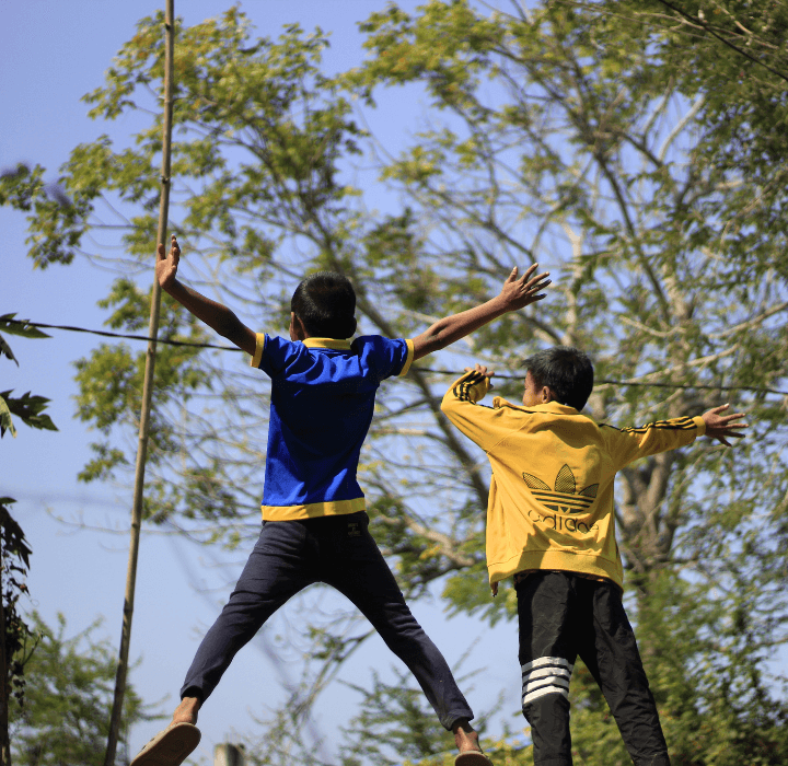 Two boys face away from the camera. They hold their arms wide and up in the air.